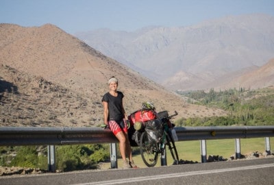 Un hombre posando con su bicicleta en el lado de una carretera.