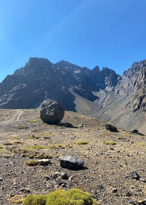 Una aventura por tierra te lleva al fascinante paisaje del Cajón Las Leñas, donde una roca solitaria se alza en medio del vasto desierto, flanqueada por majestuosas montañas al fondo.