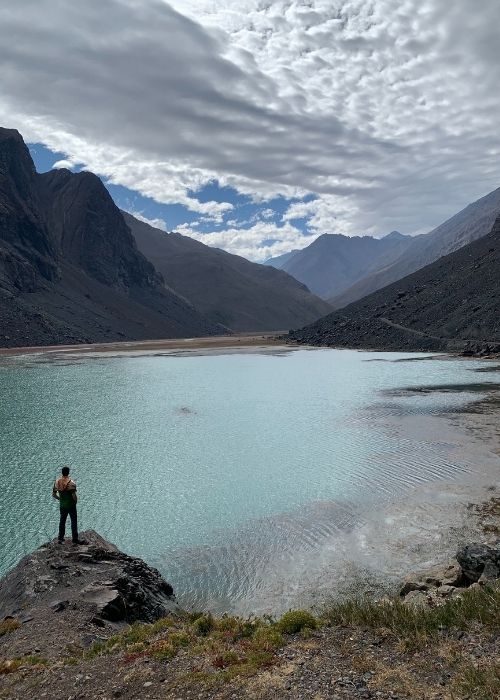 Un hombre parado frente a un lago en las montañas, cerca del Cajón Las Leñas.
