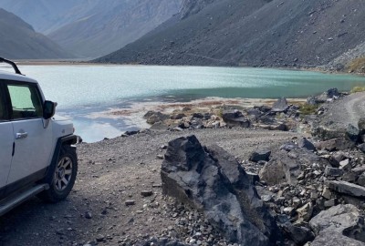 Un jeep Overland está estacionado en un camino rocoso cerca del Cajón Las Leñas, con vista a un lago.