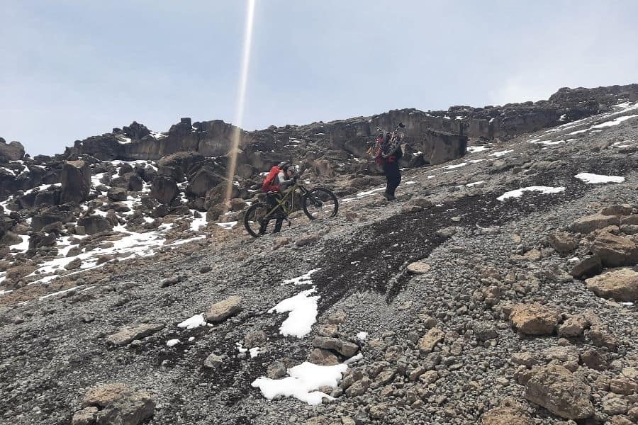 Dos mujeres poderosas subiendo en bicicleta por una montaña rocosa en África.