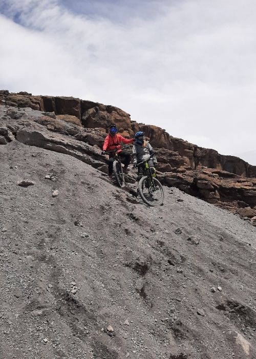 Dos mujeres conquistando una colina rocosa en sus bicicletas de montaña, mostrando su espíritu de poderosas en África.