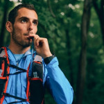 Un hombre habla por su teléfono celular mientras corre por el bosque con la hidratación adecuada.