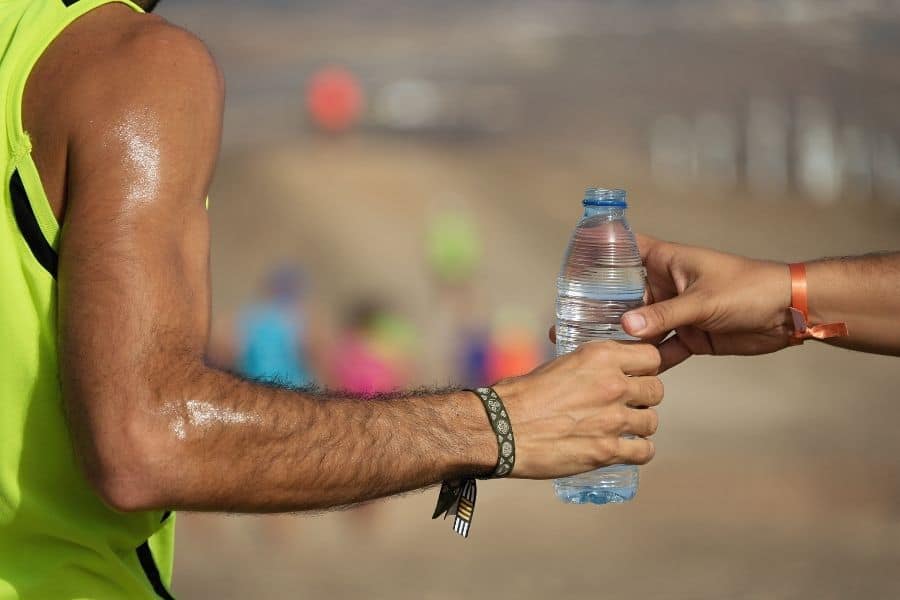 Un hombre le entrega una botella de agua a otra persona durante una carrera para que se hidrate adecuadamente.