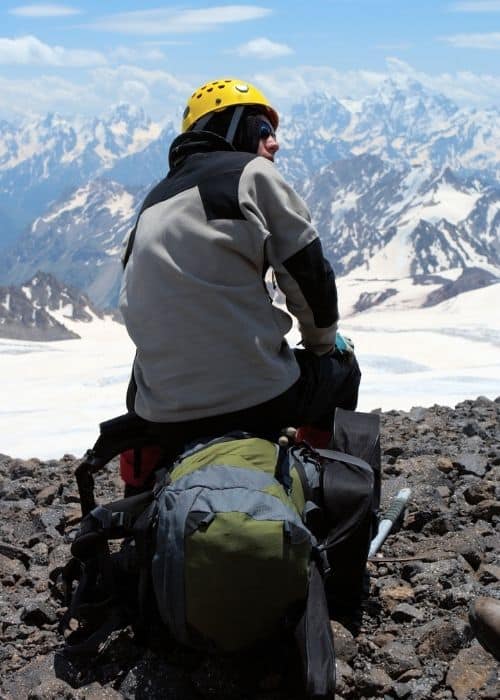 Un hombre sentado a gran altura con una mochila, experimentando los efectos de la altitud en su cuerpo y salud.