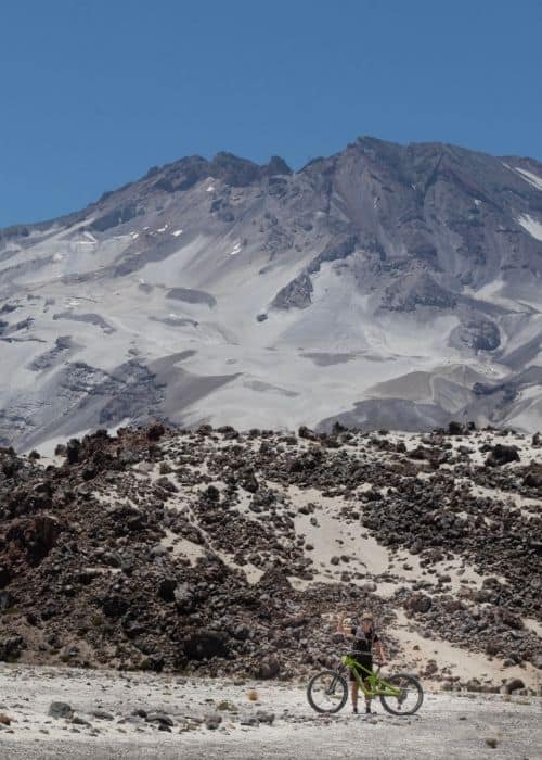 Una persona montando en bicicleta frente a un volcán nevado.