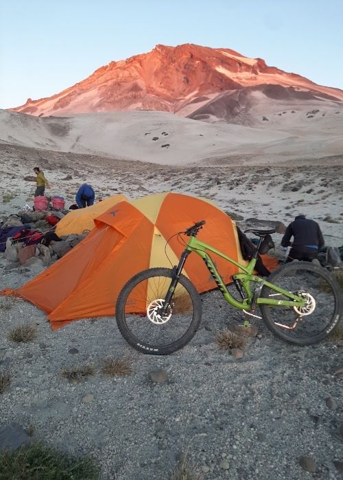 Un grupo de personas acampando cerca de una montaña con una bicicleta delante.