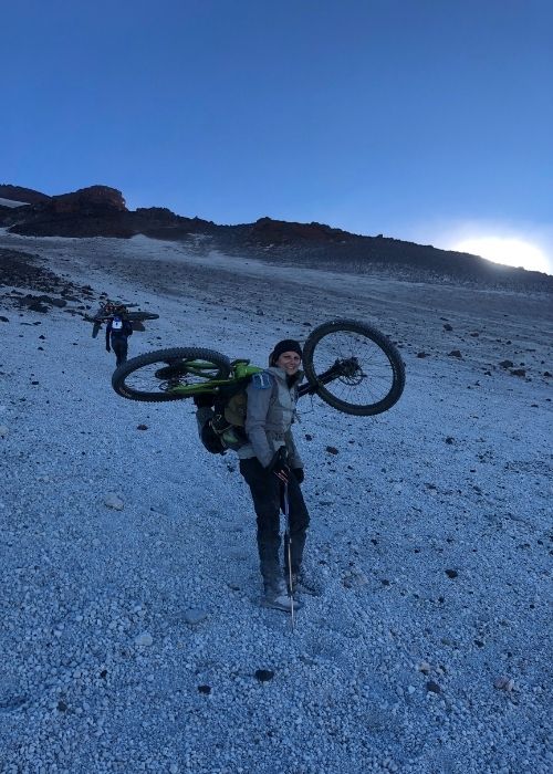 Un hombre llevando una bicicleta en una montaña nevada.