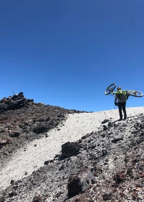 Un hombre llevando una bicicleta de montaña por una pendiente rocosa.