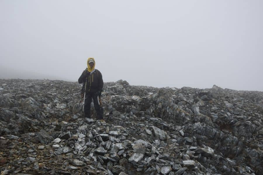 Un hombre realizando el primer ascenso en la cima de la muela en la Patagonia, de pie sobre un montón de rocas.