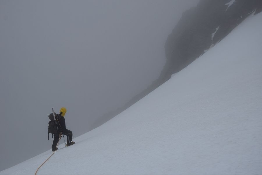 Un hombre sube una ladera nevada en la Patagonia, intentando el primer ascenso de la muela.