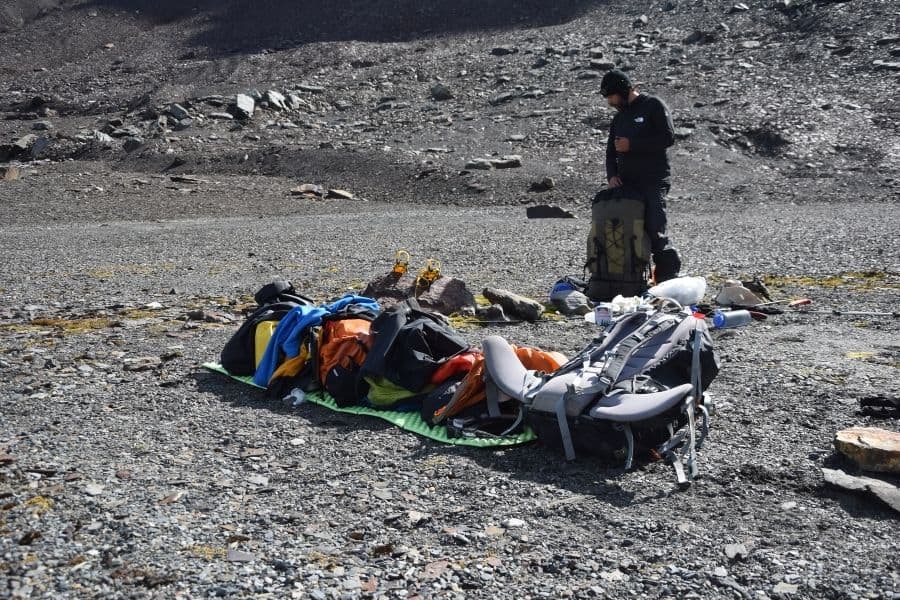 Un hombre parado junto a su mochila en una montaña rocosa durante su aventura en la Patagonia.