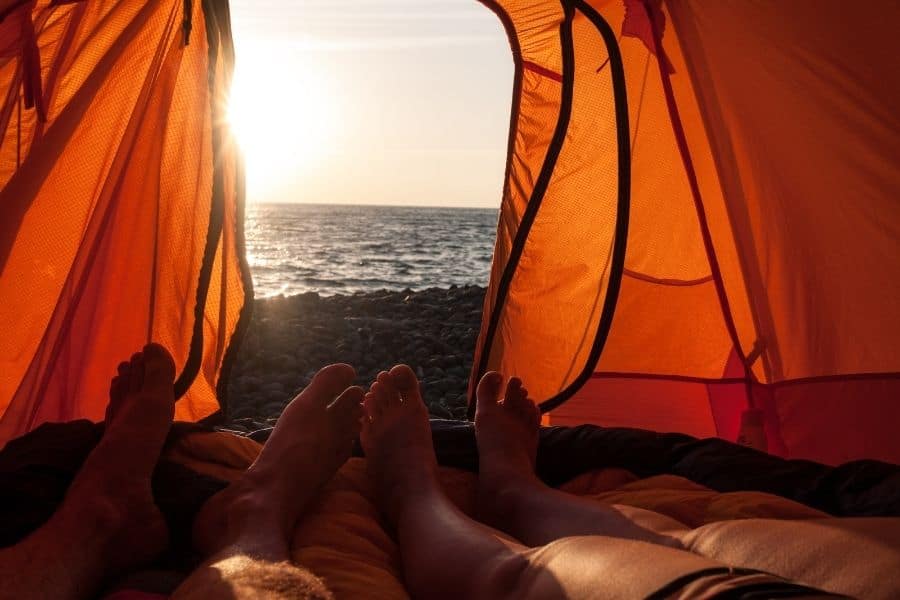 Los pies de una pareja de playeros en una tienda de campaña con vistas al océano.