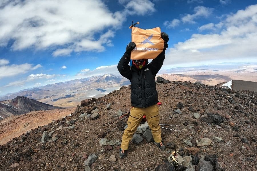 Un hombre sosteniendo una bolsa en la cima de una montaña en Chile.