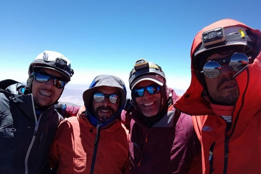 Cuatro hombres con chaquetas rojas parados en la cima de una montaña chilena.