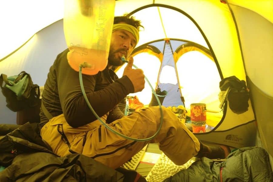 Un hombre sentado en una tienda de campaña durante el andinismo Chile6Mile, sosteniendo una botella de agua.