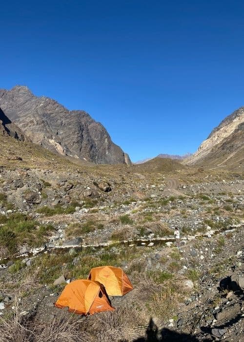 Dos mochilas instaladas en un valle con las montañas al fondo.