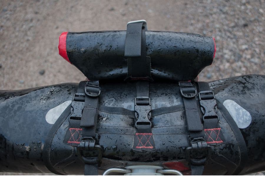 La parte trasera de una motocicleta con una mochila atada, pedaleando bajo la lluvia.