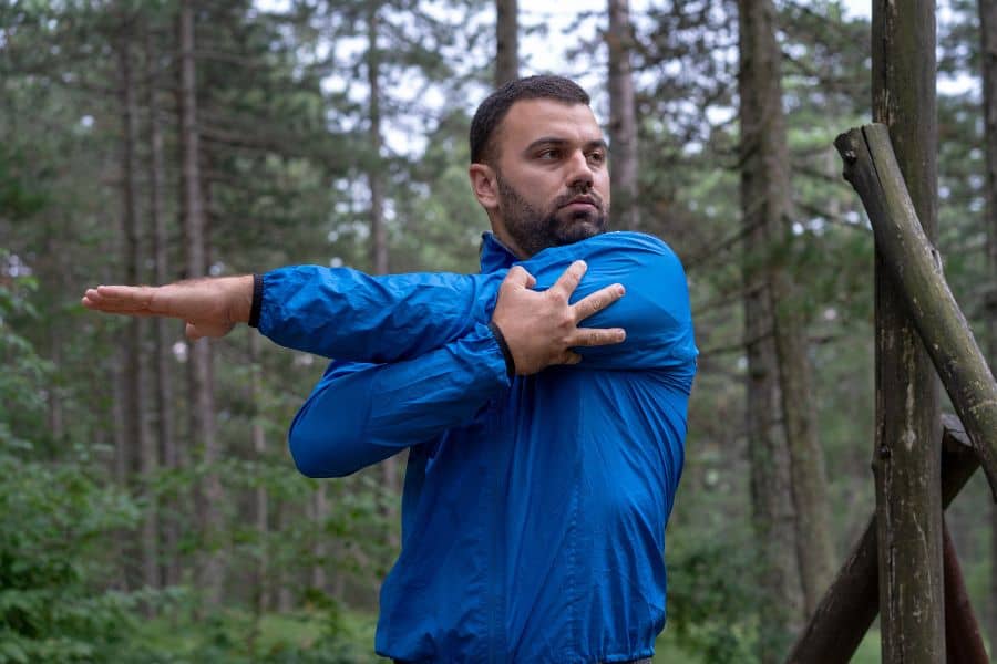 Un hombre con chaqueta azul practica artes marciales en el bosque, demostrando técnicas para evitar fatiga y lesiones durante el trekking.