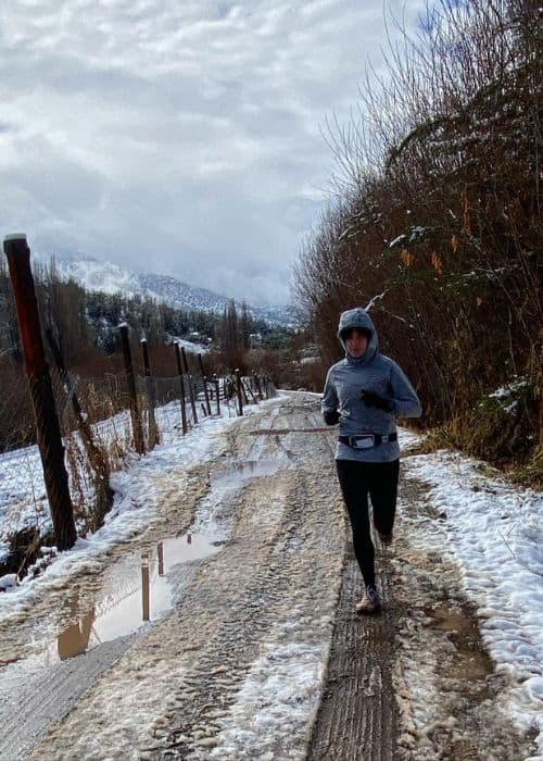 Una mujer desafiando el frío y corriendo por un camino de tierra en la nieve, aplicando consejos para entrenar con bajas temperaturas.